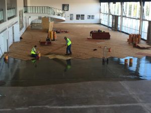 Workers installing hardwood floors in a spacious ballroom, showcasing quality craftsmanship available through the Front Range’s largest wood-focused flooring retail needs.